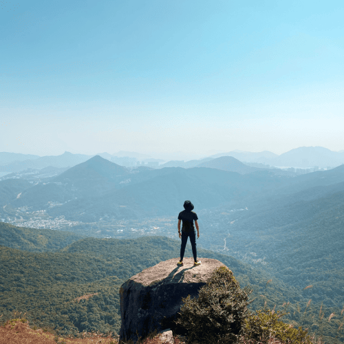 A man is standing on a rock, overlooking a scenic view of mountains and valleys under a clear blue sky.