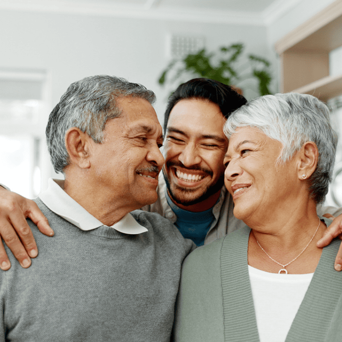 Three people are smiling and embracing each other indoors.