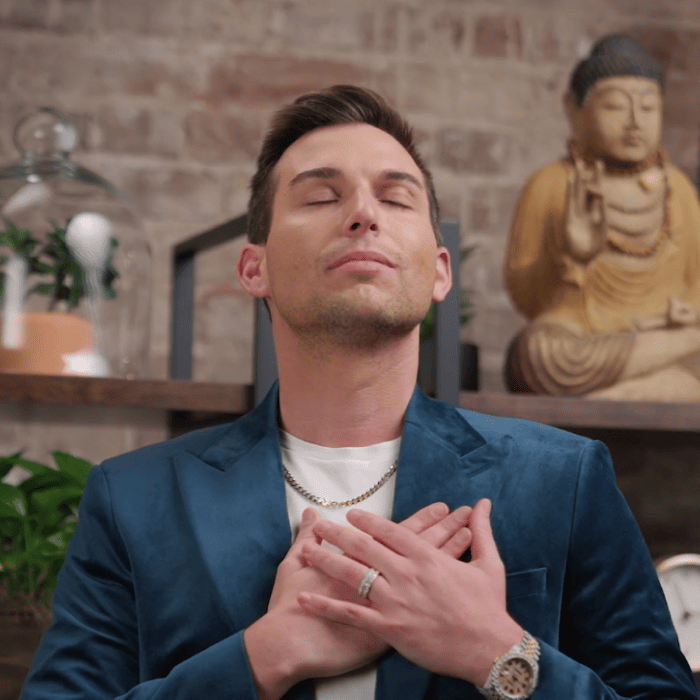 A man in a blue blazer, identified as Matt Fraser, stands with eyes closed and hands on chest, in front of shelves with plants and a Buddha statue.