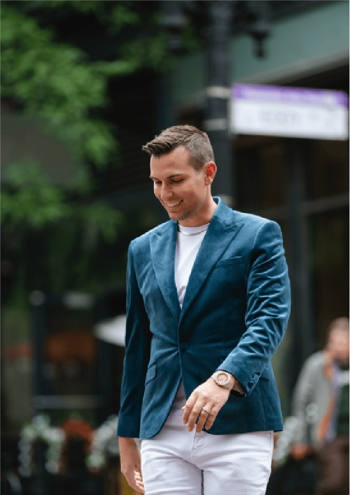 Matt Fraser, in a blue blazer and white pants, is walking outside, smiling and looking down.