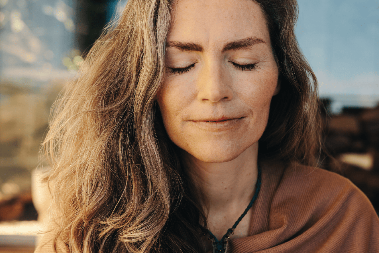 Woman with long hair and closed eyes, wearing a brown top, appears calm and relaxed.