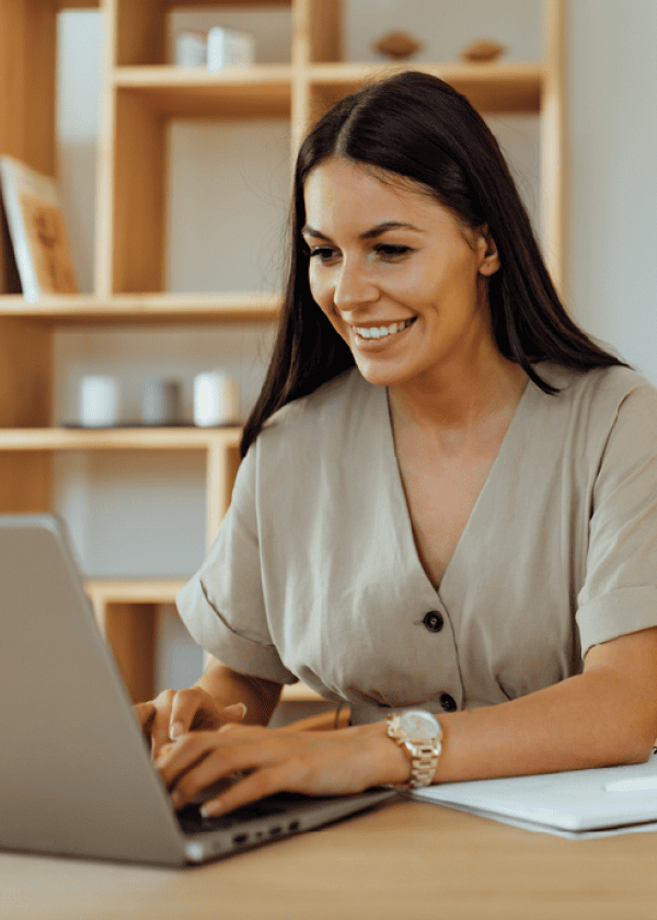 Smiling woman in a beige shirt typing on a laptop at a wooden desk, with Matt Fraser mentioned and shelves in the background.