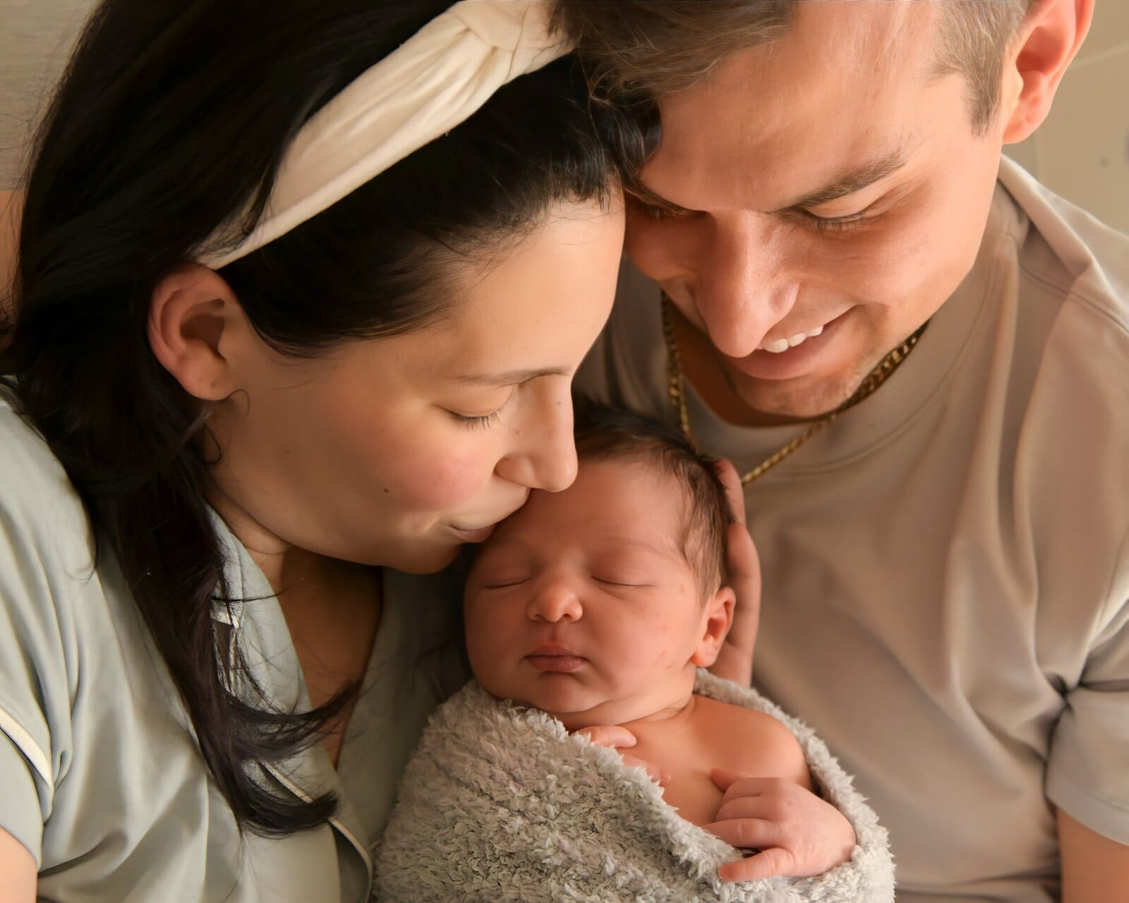 Matt Fraser & Alexa Fraser lovingly cradles their sleeping newborn wrapped in a blanket.